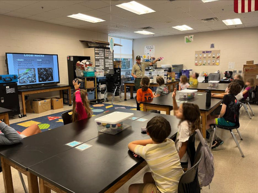 Students sitting at desks in a classroom, attentively listening to Christopher A. Toney, AML Program Specialist for Education Outreach in William H. Justice Elementary School.