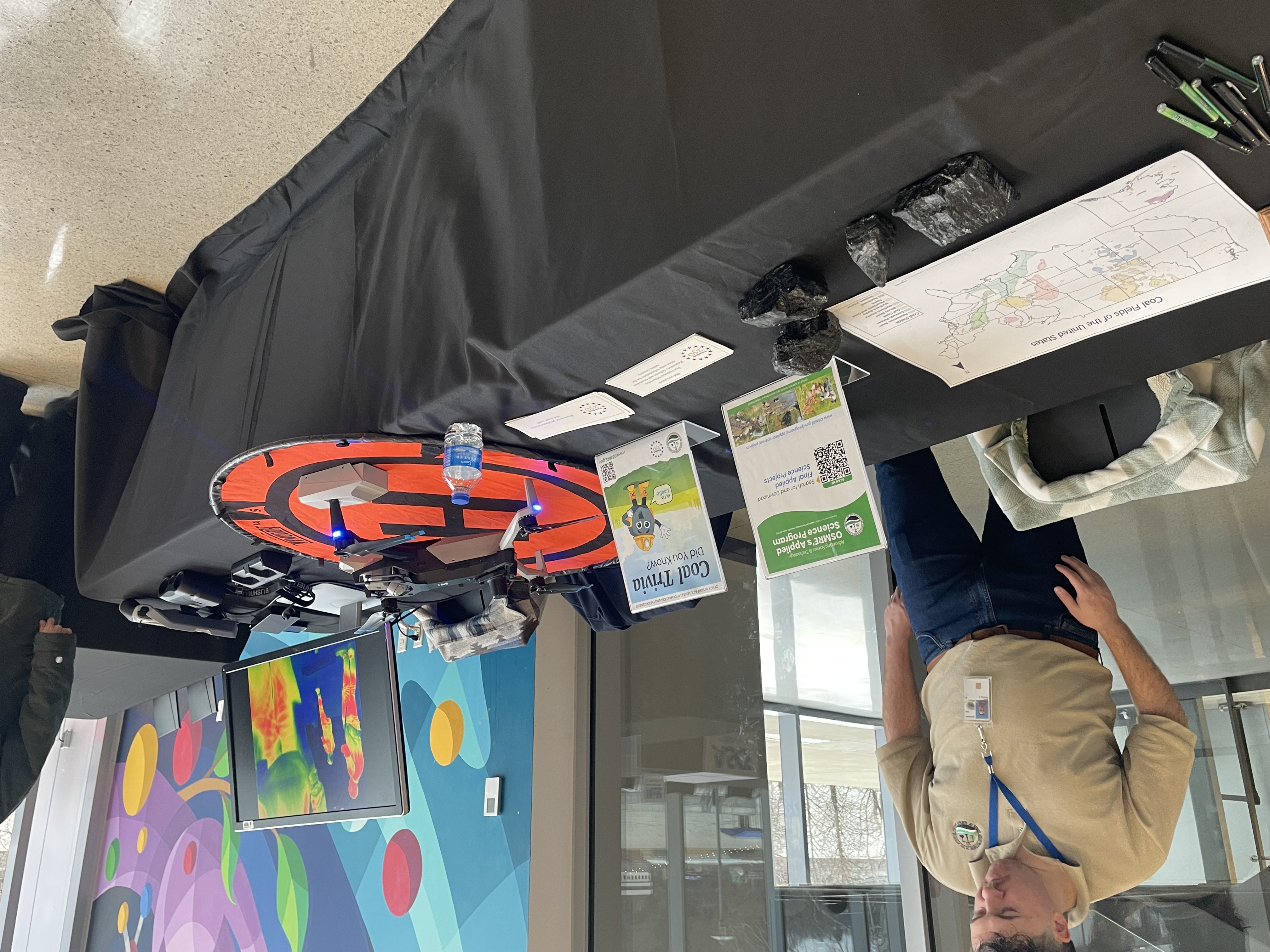 OSM geologist, Michael Behe, standing behind the OSM table showcasing a coal fields map, samples of coal, coal mine trivia, and a UAS with a thermal camera set up