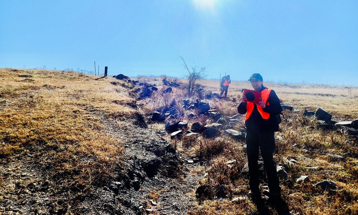 Gelareh Smith stands in work clothing in a rocky field.