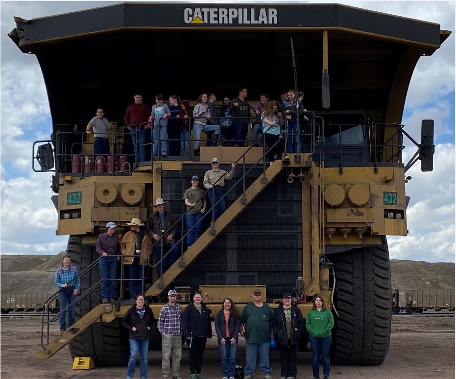 A group of high school students stand atop and in front of large Caterpillar heavy equipment at a mine site