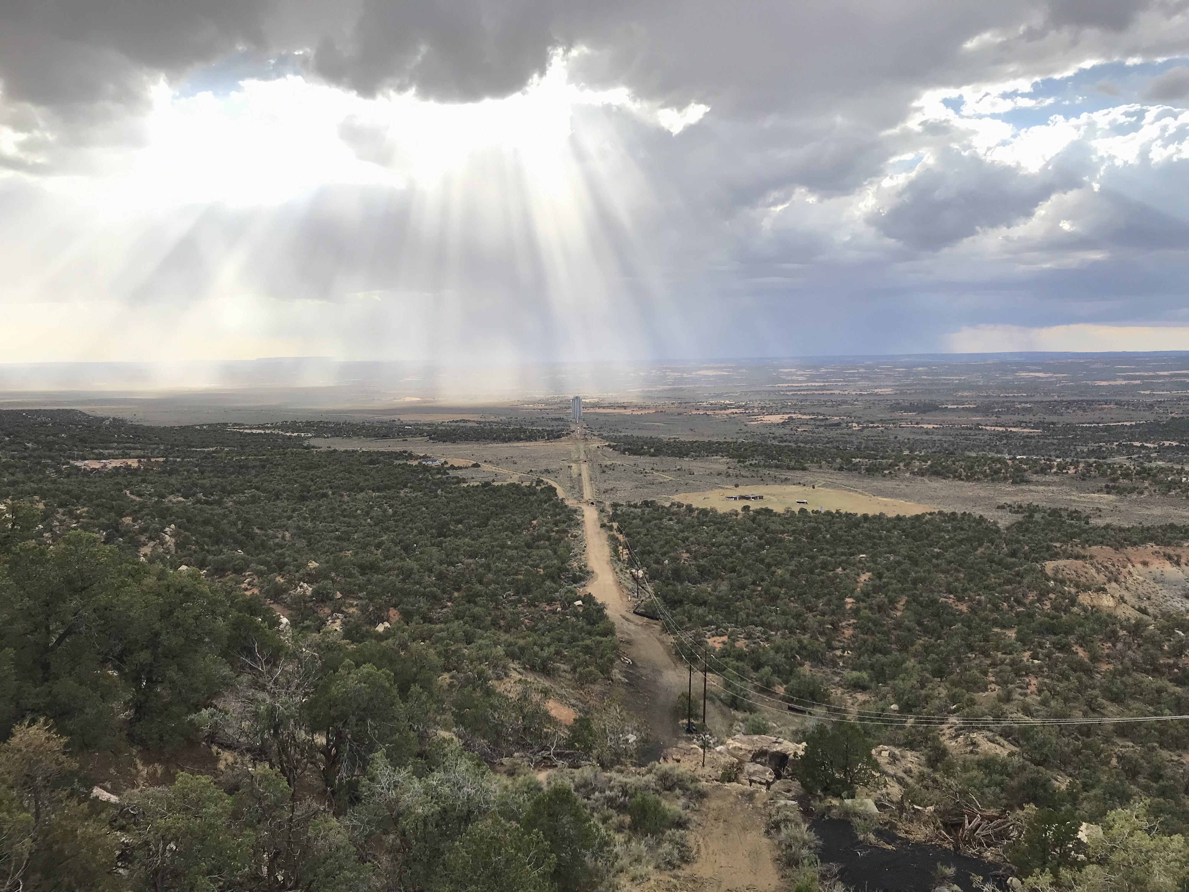 Photo showing where the coal conveyor belt line was with a mostly cloudy sky with sunbeams shining down behind the coal silo. 