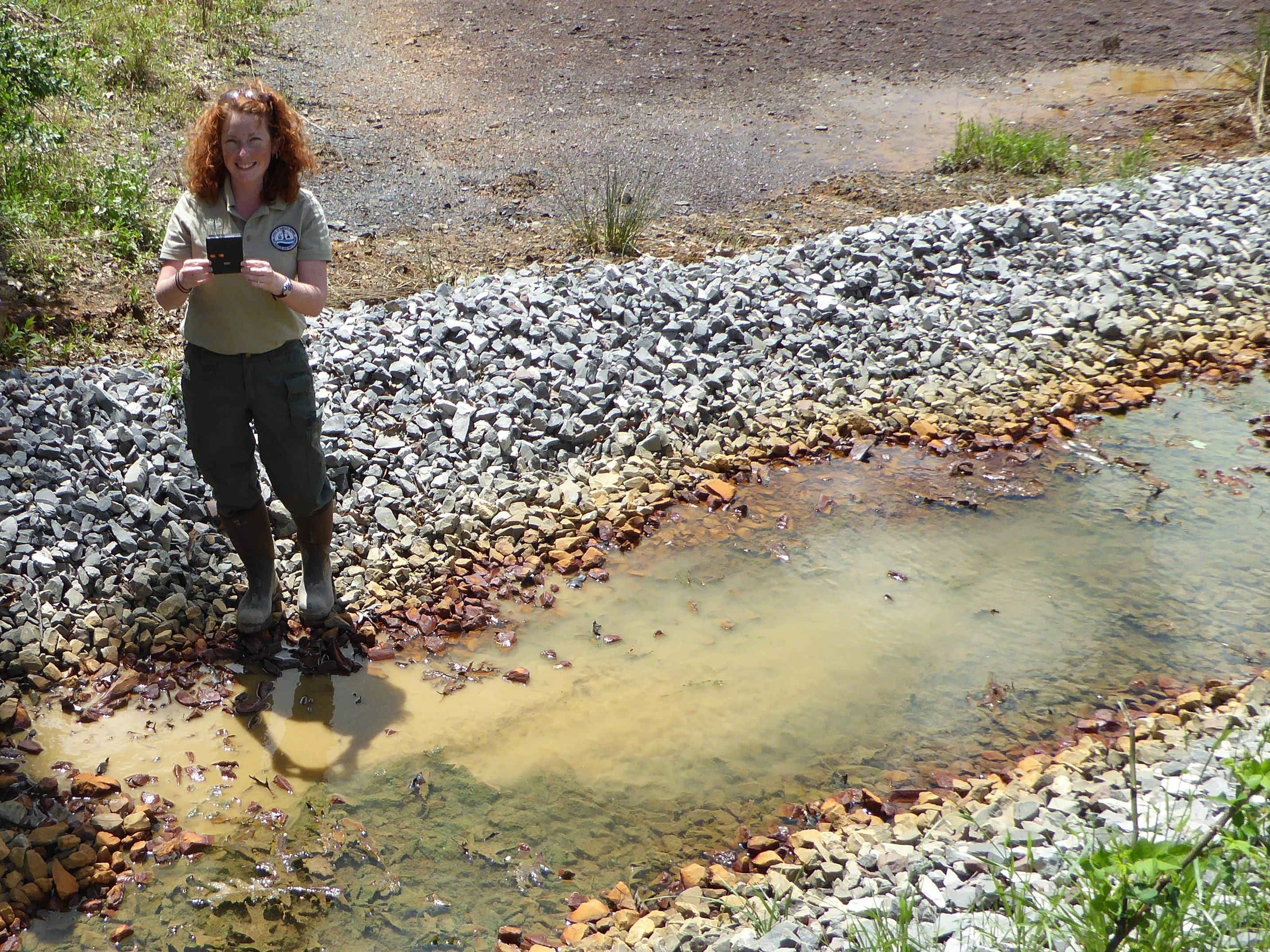 Jenna Hincks stands next to a creek holding a water sample.