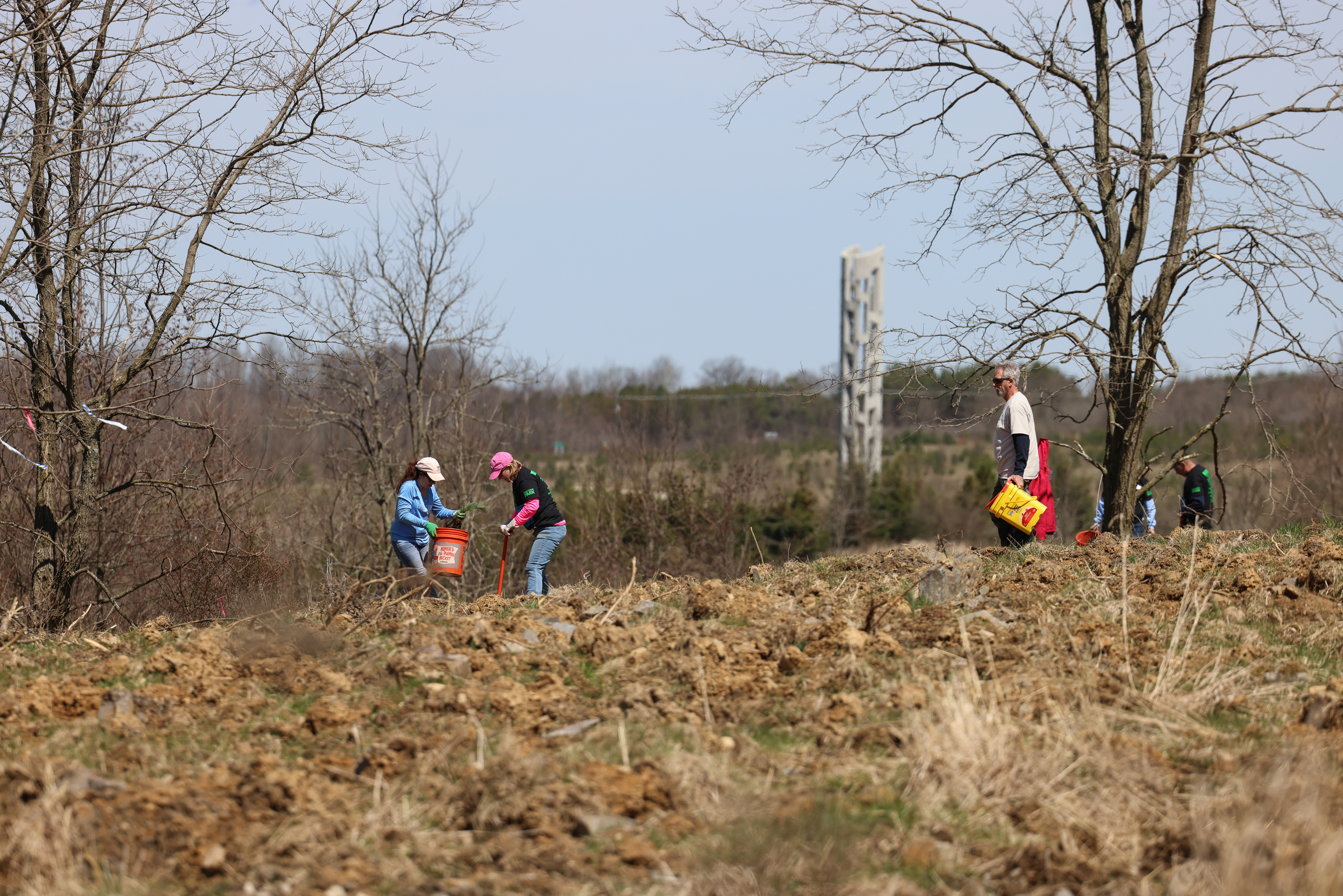 Volunteers plant trees - Tower of Voices in the background - during the Plant a Tree at Flight 93 event at the Flight 93 National Memorial, Somerset County, Pennsylvania, April 22, 2022. The event highlighted more than 10 years of work and events to plant over 150,000 trees, across 214 acres of former coal mine land. (Photo courtesy of NPS/B. Torrey)