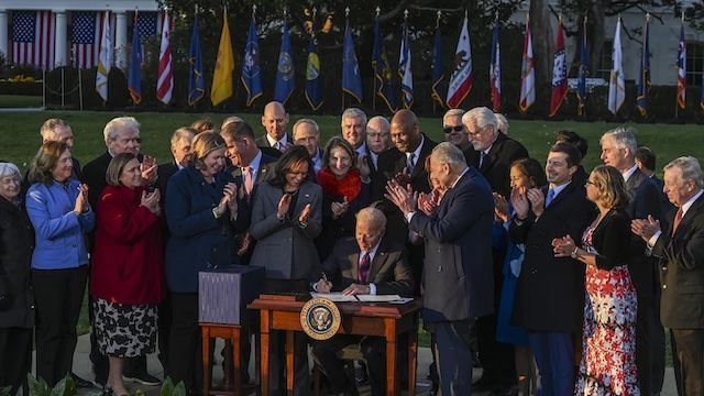 President Biden signs the Infrastructure Investment and Jobs Act as he is surrounded by lawmakers and members of his Cabinet during a ceremony on the South Lawn at the White House