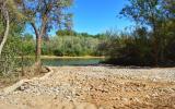 Sand and rocks sit in the foreground of a waterway vista surrounded by trees and blue sky