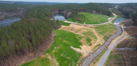 An aerial view shows evergreen woods, waterways, and meandering roads through fresh green grassy areas of a Bibb County, AL reclamation area.