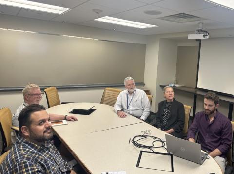 Staff seated in a meeting room during a virtual session on improving geospatial workflows using tools to support abandoned mine land programs and SMCRA compliance.