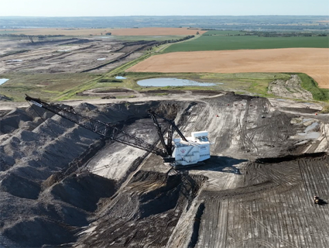 Distant overhead shot of a large mining machine with a boom arm extended over a cut in the earth